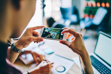 Akıllı telefon cihazını tutan ve üretken ve etkili çalışma için masaüstünde resim çizen, kurslara hazırlanırken dijital cep telefonunda grafiğin fotoğrafını çeken kesilen eller.
