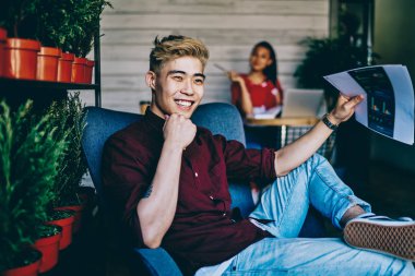 Rahat kot giymiş neşeli gülümseyen genç adam bilgi analiz mola sırasında gülerek elinde grafik verileri ile kağıt kroki tutan kağıt kroki giymek, Çinli hipster adam loft kafede iyi hissediyorum