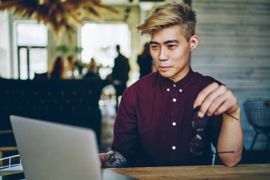 Başarılı Asyalı hippi, kafeteryada yüksek hızlı internet bağlantısı kullanarak, uzaktan kumandayla modern dizüstü bilgisayarda çalışıyor.