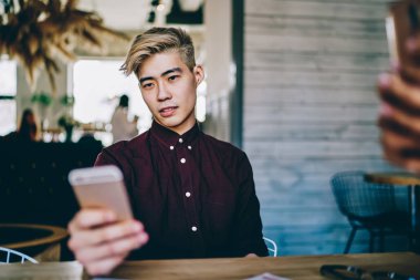 Japon hipster adam akıllı telefon cihazında uygulama bildirimi okuyor, Asyalı erkek blogcu modern cep telefonuyla interneti taramak için 4G kablosuz kullanıyor.