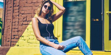 Cep telefonu kulaklıkları ve medya uygulaması ile dinleme müzik parçaları sırasında reklam alanında dinlenmek trendy güneş koruyucu kız, Genç kadın motivasyon ses kitabı zevk