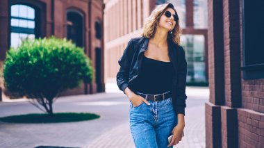 Happy hipster kız Casual giyim gülmek ve güneşli bahar günü sırasında hafta sonu zevk giyinmiş, trendy güneş gözlüğü kenara bakarak ve gülümseyen şehir etrafında gezinirken neşeli kadın genç