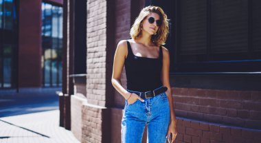 Güneşli yaz gününde kentsel ayarı üzerinde arkadaş bekleyen güneş gözlüğü pozitif hipster kız, tanıtım alanında şık kıyafet ayakta çekici beyaz kadın genç ve eğlence zevk