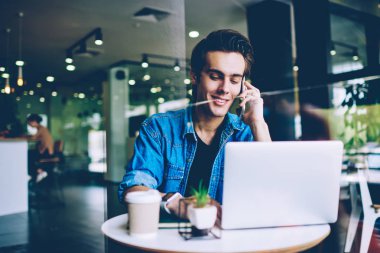 Gülümseyen erkek öğrenci dizüstü bilgisayar üzerinden şakalar ile komik web siteleri ararken olumlu telefon görüşmesi yaparken, mutlu adam cep telefonu üzerinden arama ve modern netbook e-posta yazarak