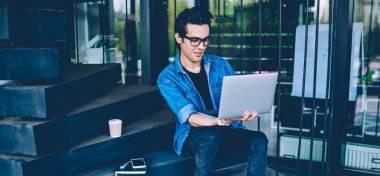 Optik gözlük pozitif hipster adam dizüstü bilgisayarda uygulama üzerinden video online izlerken, başarılı erkek freelancer sunum oluşturmak için netbook üzerinden multimedya dosyaları arıyor