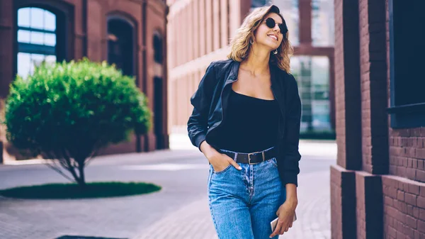 Happy hipster kız Casual giyim gülmek ve güneşli bahar günü sırasında hafta sonu zevk giyinmiş, trendy güneş gözlüğü kenara bakarak ve gülümseyen şehir etrafında gezinirken neşeli kadın genç