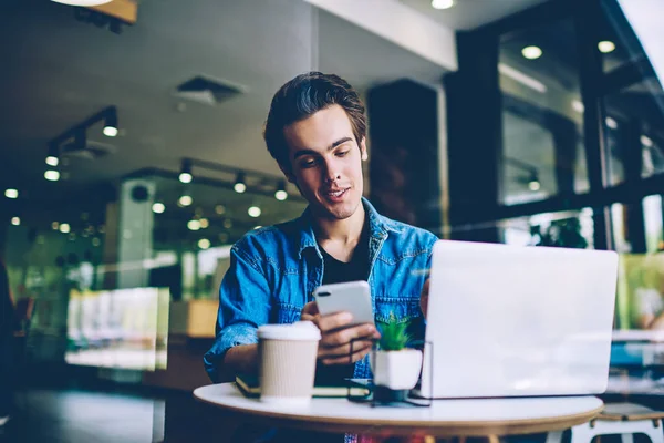 Mutlu bin yıllık hipster adam iletişim için mobil uygulama kullanarak arkadaşlarınızla mesajlaşma, arama için iletişim numarası ararken kafeteryanetbook ile oturan başarılı erkek öğrenci