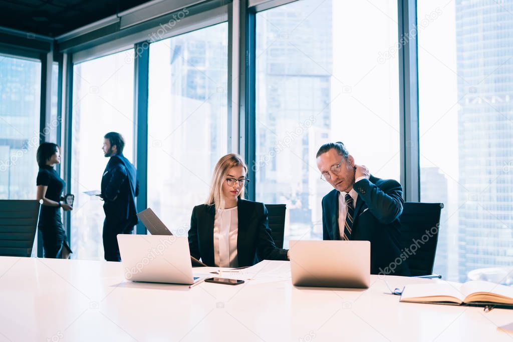 Intelligent male and female proud ceo checking information from laptop during collaboration meeting in office interior, corporate financial employees working with computers at table, business partners