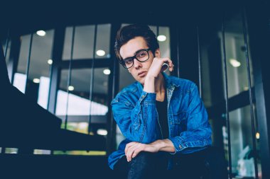 Optik gözlük yakışıklı ciddi hipster adam kentsel oturma oturan ve hayat hakkında düşünürken arkadaşı dışarıda beklerken, kot giyim genç kafkas adam kampüste düşünme hissi
