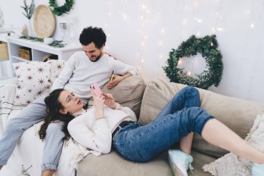 Milenyum hipster 'ı kış tatilinde kız arkadaşına akıllı telefondan uygulama gösterip kanepede uzanmış, birbirine aşık çift cep telefonu ve bluetooth kullanarak multimedya içeriğini paylaşıyor.