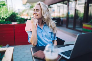 Elinde not panosuyla, modern bir açık hava barının masasında oturmuş kahve molası verip bakışlarını başka yöne çevirerek toplantıyı bekliyor.