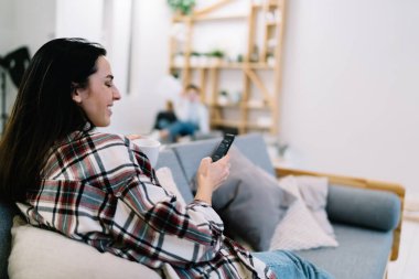 Rahat koltukta oturan ve evde vakit geçirirken cep telefonunu karıştıran neşeli kadın manzarası