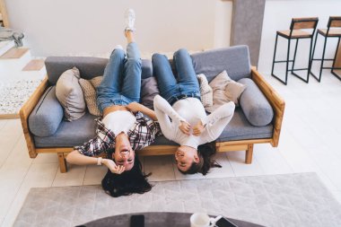 Evdeki rahat oturma odasındaki modern kanepede dinlenirken gülen gündelik giysiler içindeki genç kadınlardan.