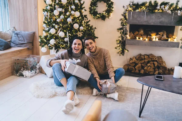 Sıcak süveter giymiş, süslenmiş köknar kutularıyla birlikte oturan ve kameraya bakarken gülen kadınların olduğu yerden.