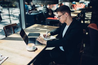 Yukarıdan bakıldığında, iş projesinde çalışırken notlar yazan ve dizüstü bilgisayar kullanan odaklı genç işadamlarının bakış açısı