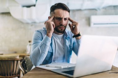 Genç, stresli erkek, dizüstü bilgisayarla kafenin önündeki masada otururken konsantrasyonla düşünüyor.