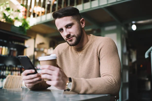 Hombre Barbudo Guapo Usando Teléfono Móvil Sosteniendo Taza Café Mientras —  Fotos de Stock