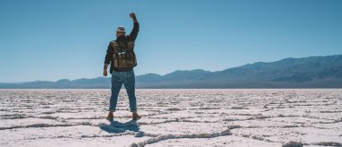 Aktif giyinmiş, hafta sonları vakit geçirirken büyük dağların önünde dikilen isimsiz erkek yürüyüşçünün arka görüntüsü.