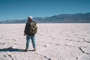 Sırt çantalı, sıcak elbiseli, mavi gökyüzüne karşı boş duran kimliği belirsiz bir erkeğin yan görüntüsü.