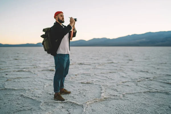 バックパックと手に写真カメラ付きの男性ハイカーのフルボディ離れて見て Badwater Basinに位置する山の写真を撮る — ストック写真