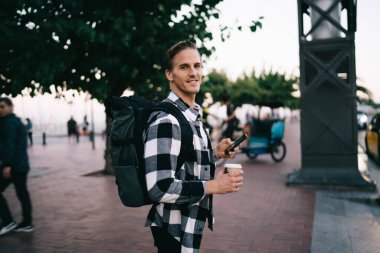 Sırt çantalı, gezgin, sokak ziyaretinde cep telefonu kullanan, akıllı telefon rezervasyon taksisinde telefon eden, kameraya bakan, gülümseyen beyaz adam portresi.