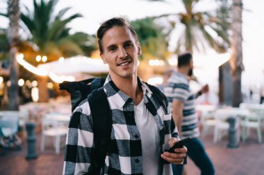 Sıradan giyinen yakışıklı bir adamın yarım boy portresi gezici bağlantı üzerinden sohbet etmek için cep telefonu taşıyor, 20 'li yaşlarda hippi bir gezgin kameraya bakıyor.