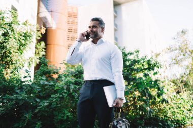 Resmi giyinmiş orta yaşlı işadamı, operatörle dijital akıllı telefondaki banka hesabı hakkında konuşurken, yetişkin girişimcinin internet üzerinden telefon görüşmesi için gezinen internet bağlantısını kullandığından emin.