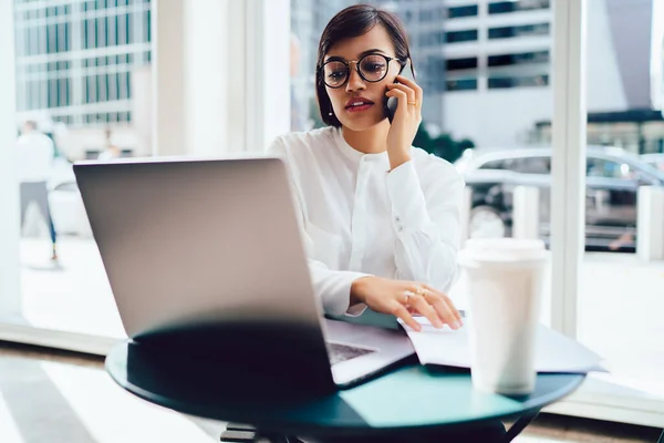 격식있는 안경을 여성이 노트북을 스마트폰으로 대화하면서 사무실에 — 스톡 사진