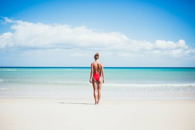 Mauritius adasında güneşli bir günü kumlu tropikal plajda geçirdiği için seyahatin tadını çıkaran genç, sıska gezgin, Kuba 'da güneşlenirken kırmızı mayo giyen bayan turist