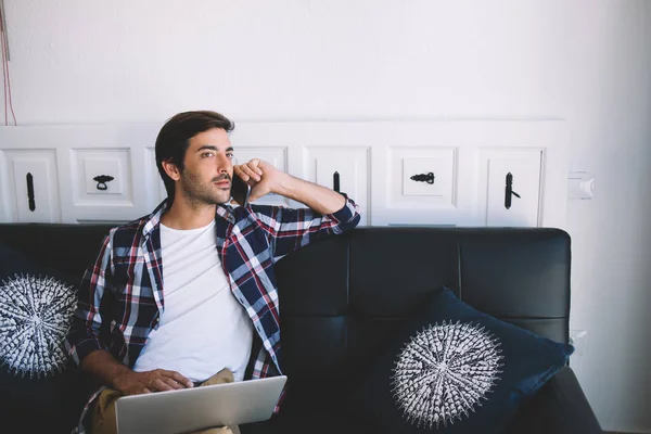 South Asian programmer calling to remote partner for discussing software update on laptop technology, skilled male freelancer working remotely on business project consultancy via mobile device