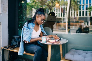Ciddi esmer tenli kadın öğrenci, modern teknolojiyi kullanarak internet üzerinden kitap okumayı öğreniyor. Düşünceli Afro-Amerikan kadın blogcu, dijital tablet ile kafeterya terasında oturuyor.