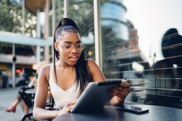 Gülümseyen koyu tenli kadın blogcu modern dijital tablet üzerinden haber okuyor, Afro-Amerikan kadın milenyum video izliyor ve sosyal ağlarda iletişim kuruyor.