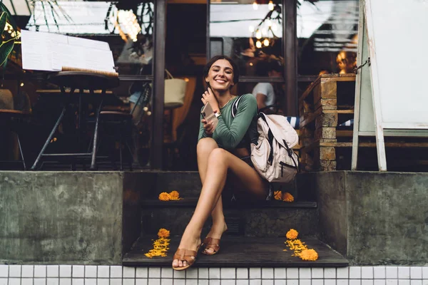 ストリートにあるモダンなカフェの階段で休んでいる間 カジュアルな服を着て笑顔でカメラを見ている長さの陽気な女性 — ストック写真