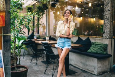 Kendine güvenen serbest çalışan kadın masaların yanında duruyor ve iş sırasında yaratıcı mekanda vakit geçirirken akıllı telefondan yeni proje hakkında sohbet ediyor.