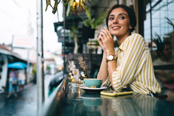 スマートフォンやコーヒーを片手にテーブル席に座り 自由な時間を楽しむカジュアルな服を着た笑顔の女性 — ストック写真
