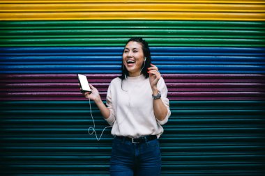 Heyecanlı Asyalı kullanıcı boş telefonuyla reklam alanında sırıtıyor komik sesli podcast dinlemek için boş zamanından memnun, kulaklıklı neşeli bir kadın coppy Space alanında gülüyor ve seviniyor.