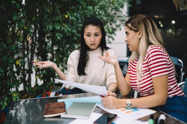 İşletme projeksiyonları için çözümler tartışan İspanyol serbest çalışan meslektaşla birlikte kağıt analizi yaparken kafası karışmış Asyalı kadın. Sınavlara hazırlanan çeşitli öğrenciler.