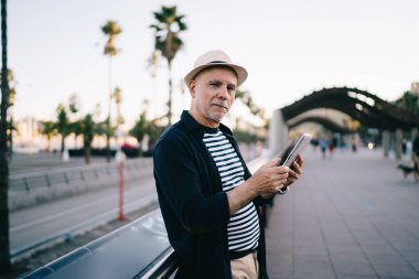 Sokakta yürürken tırabzan kenarında durup tablet kullanan yetişkin erkek turistin yan görüntüsü