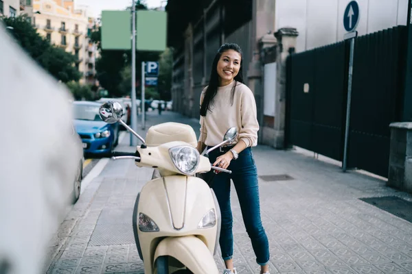 レトロなバイクで休暇の冒険を運転する準備ができている都会の通りで喜んでカジュアルな服を着た面白い女性観光客 ヴィンテージのレンタルオートバイの近くで笑うおもちゃのアジアのヒップスター女の子 — ストック写真