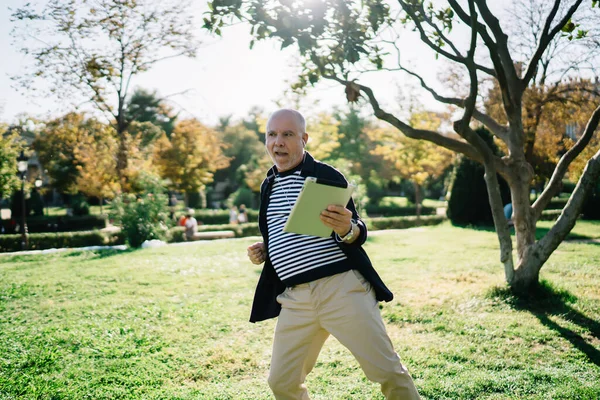 Neşeli orta yaşlı adam, günlük kıyafetleriyle çimenlerde dans ederken tablette kulaklıklarla müzik dinliyor ve gözlerini kaçırıyordu.