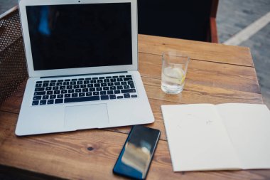 Yukarıdan bakıldığında cep telefonlu dizüstü bilgisayar ve boş günlük kaldırım kafeteryasında bir bardak suyla ahşap masa üzerinde.
