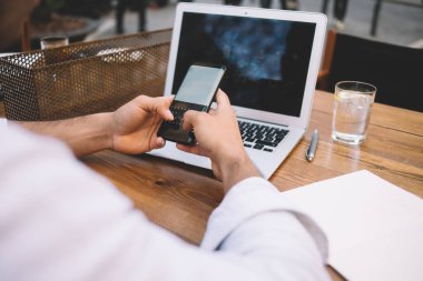 Tanımlanamayan erkek serbest yazar, tahta masada dizüstü bilgisayarla oturuyor ve güneşli bir günde açık hava kafede boş ekranlı akıllı telefonlara bakıyor.