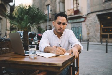 Şık giyinmiş ciddi bir erkek çalışanın yeni çalışma programı geliştiriyor ve açık uzay kafeteryasındayken not defterine bilgi yazıyor.