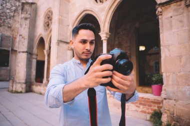 Düşünceli, gündelik giysiler içinde genç bir adam tarihi eserleri görüyor ve fotoğraf çekiyor. Gezide eski bir tarihi binanın avlusunda dikiliyor.
