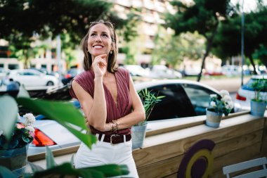 Kafe terasında durup hafta sonları boş vakit geçiren neşeli, modaya uygun giyinmiş bir kadının yarım boy portresi. Güzel bir kadın restoranda dinlenen küçük bir işletmeye sahip olmanın hayalini kuruyor.