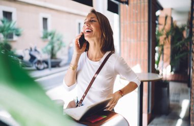 Orta yaşlı esmer, gündelik giysiler içinde cep telefonuyla konuşuyor ve kahkahalar atıyordu. Kafe dışındaki küçük masada elinde defterle duruyordu.