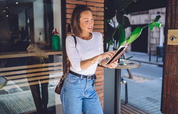 ノートブックチェックプランやアイデア付きのカフェテラスに立つカジュアルな服装で笑顔の白人女性 コーヒーブレイクで面白い本や文学を楽しんで肯定的なかなり女性 — ストック写真