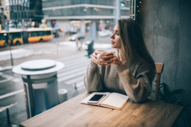 Kahvesini ısıtan düşünceli bir kadın. Boş zamanlarında kafeteryanın penceresine bakıp blog içeriği oluşturmaya çalışıyor. Kafeteryada organizasyon planlaması üzerine kafa yoran düşünceli bir kadın.