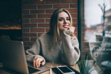 Elektronik kulaklıklı neşeli serbest yazar portresi, uzaktan işten keyif alan başarılı beyaz bilişim uzmanı mobil uygulama üzerinden pozitif müzik dinlerken kameraya gülümsüyor.