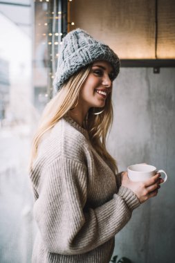 Neşeli, modaya uygun giyinmiş, kahve fincanı ile gezen, sıcak içecek içen, elinde sıcak çay tutan ve kafeterya penceresinin yanında gülümseyen Kafkasyalı mutlu bir kız.